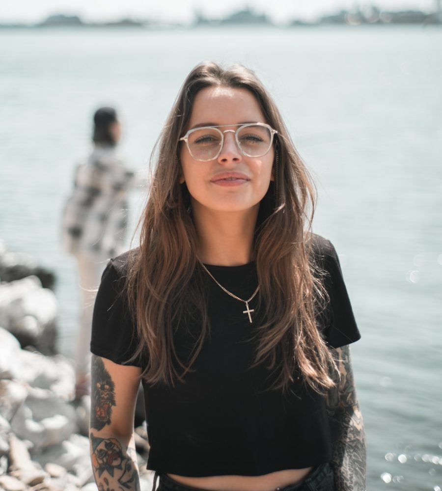 woman in black crew neck t-shirt wearing brown framed eyeglasses standing on rocky shore during
